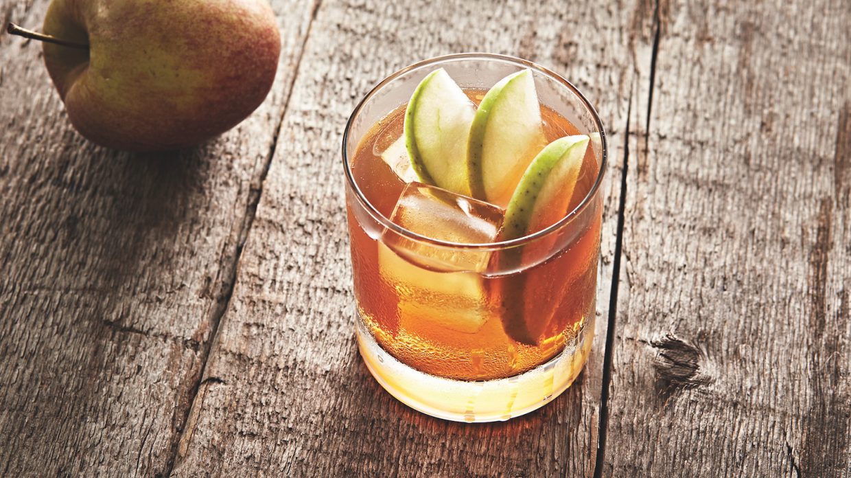 rocks glass with ice cubes and three apple slices in whiskey cocktail