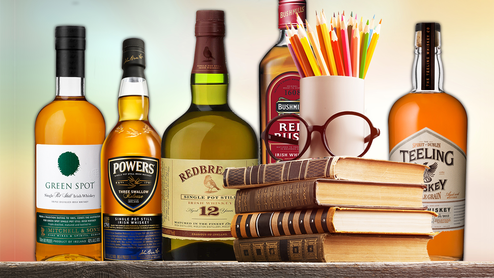 bottles of Irish whiskey arranged with a stack of books, eyeglasses, and a cup of pencils