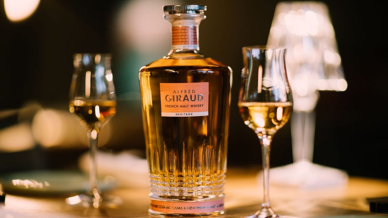 A bottle of Alfred Giraud Heritage French blended malt whisky with two stemmed tasting glasses.