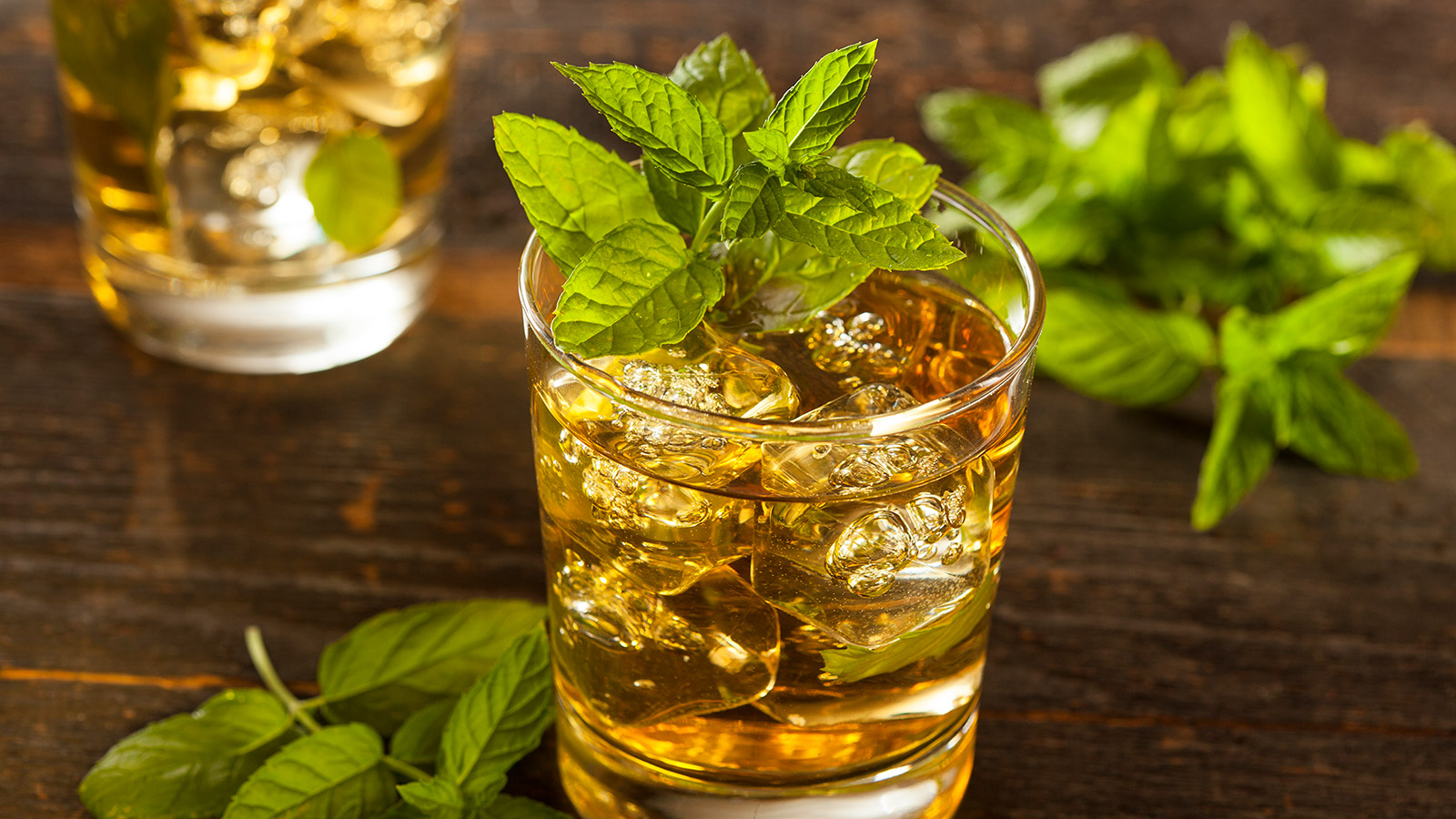 A cocktail garnished with fresh mint resembling The Howdie's Dram whisky punch rests atop a wooden surface, next to more fresh mint.