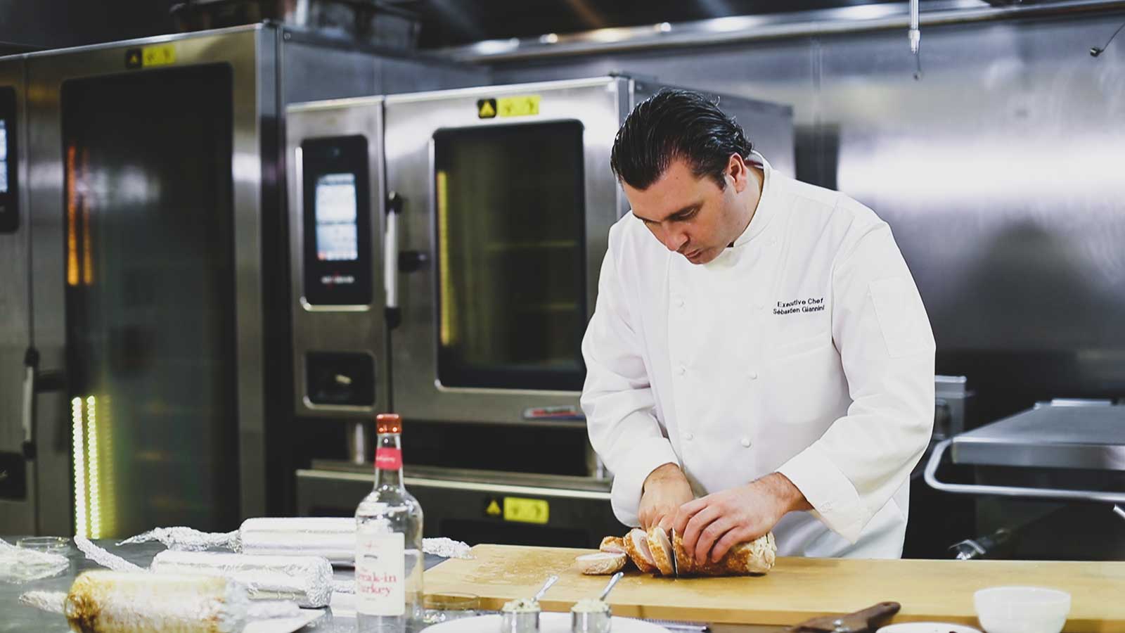 Sébastien Giannini, executive chef at Kingbird restaurant at the Watergate Hotel in Washington, D.C., slices a turkey roulade atop a cutting board in a restaurant kitchen.