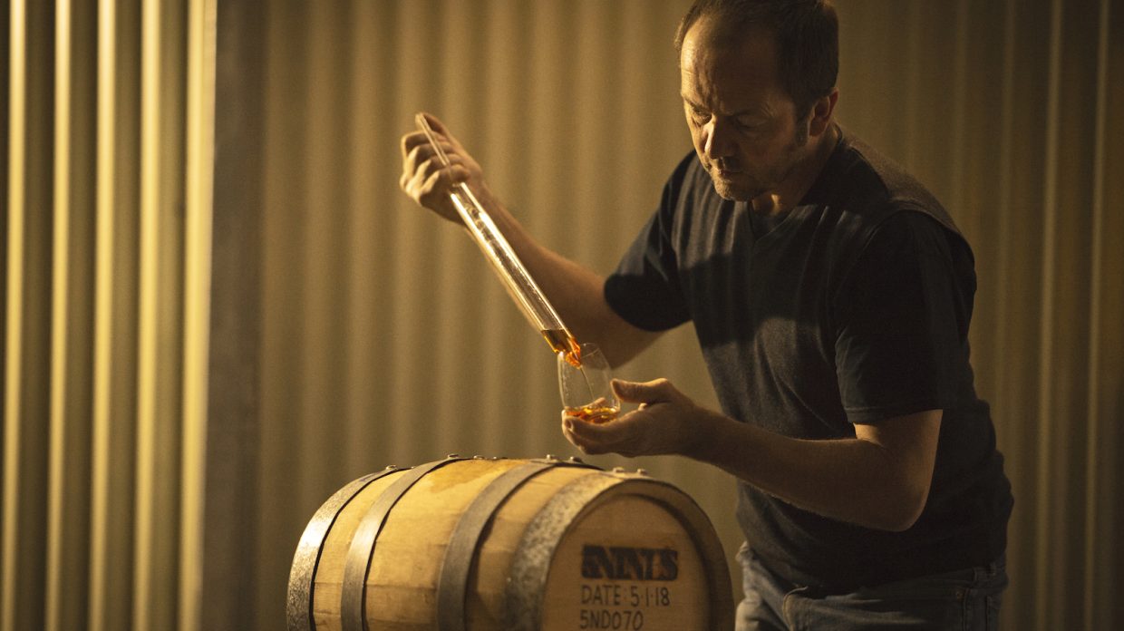 A man pipes whisky from a barrel to a glass.