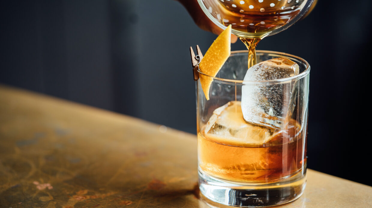 A whiskey cocktail being poured into a rocks glass.