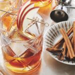 Two whiskey cocktails sit next to a small plate of cinnamon sticks.