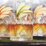 3 whiskey cocktails garnished with apple slices on a platter.