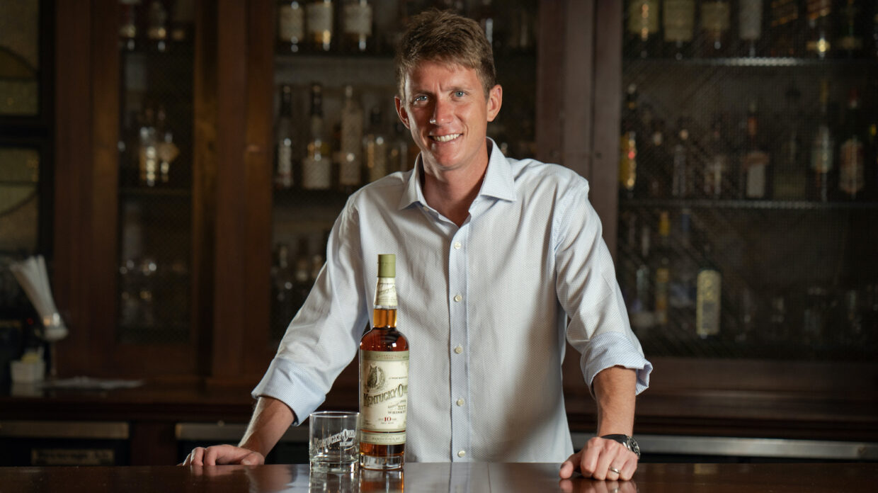 Dixon Dedman stands behind a bar with a bottle of Kentucky Owl.