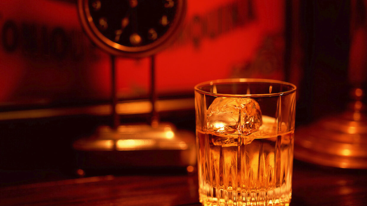 A glass of whisky in front of a desk clock.