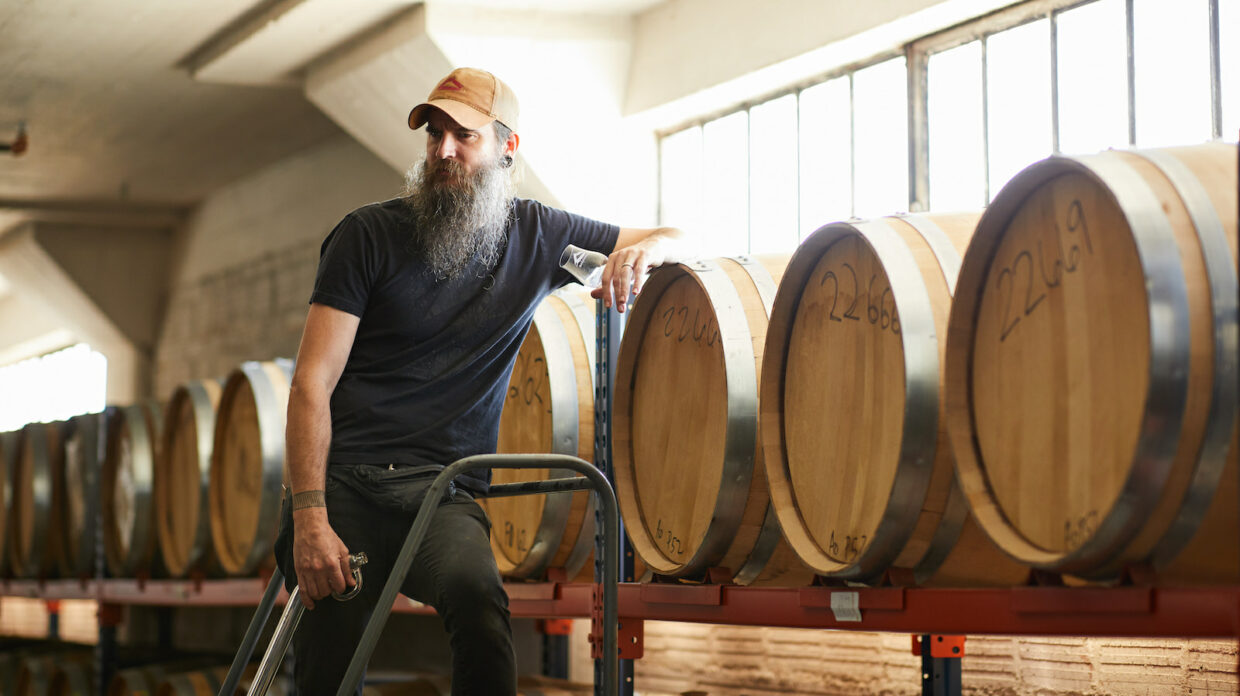 A man stands in a barrel warehouse taking samples.