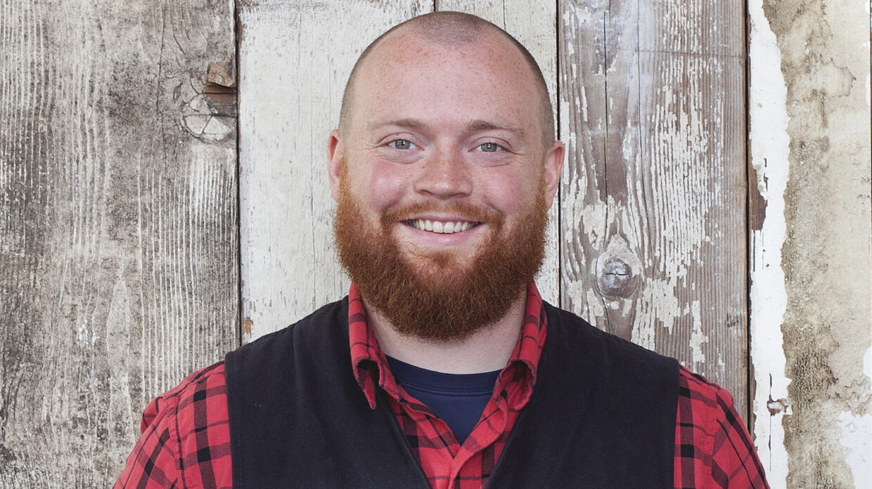 Bearded man smiles in front of wood planks in the background