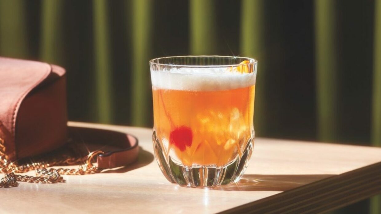 Whiskey sour cocktail on a wooden table with a green background