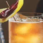 a cocktail with a pepper and lemon garnish