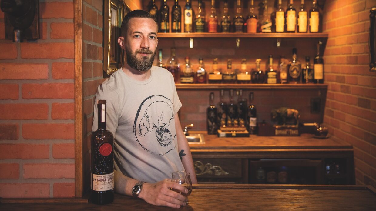 A man poses with a whiskey glass in front of his home bar